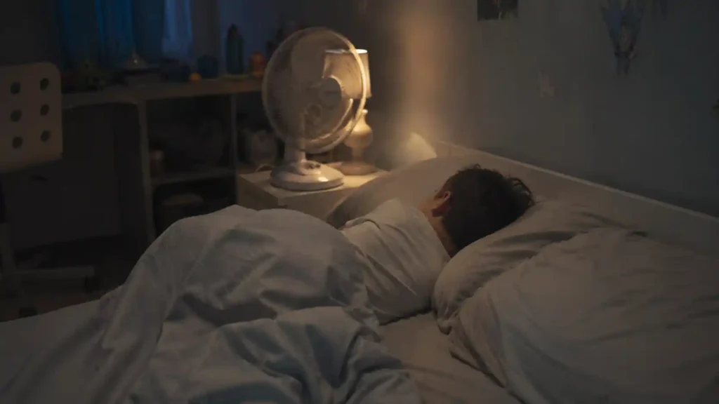 Child sleeping peacefully in a bedroom on a hot night with a fan and light bedding